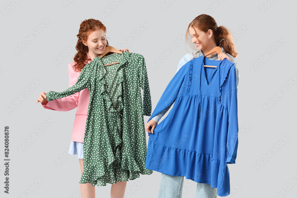 Happy redhead sisters with stylish dresses on grey background