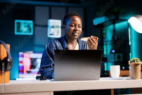 Smiling woman using credit card for online purchases, making internet transactions while shopping from her apartment. Black lady buying goods, e commerce internet banking, and spending money. photo
