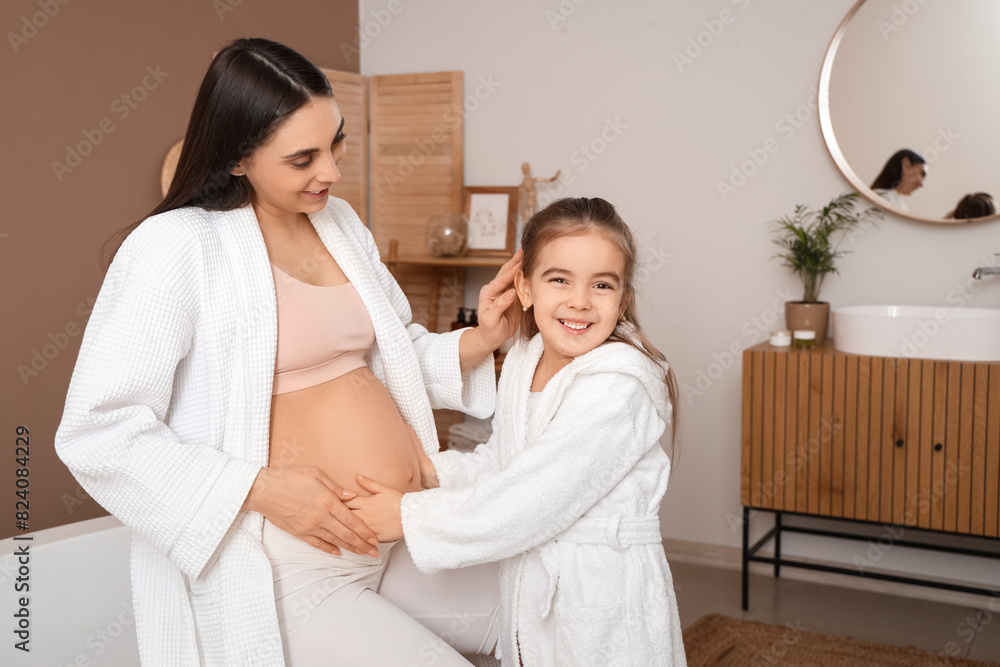 Little girl touching belly of her pregnant mother in bathroom