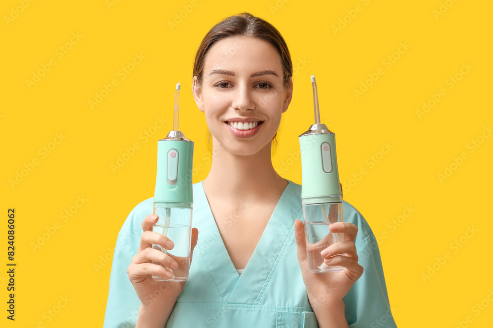 Female dentist with oral irrigators on yellow background Female dentist with oral irrigators on yellow background