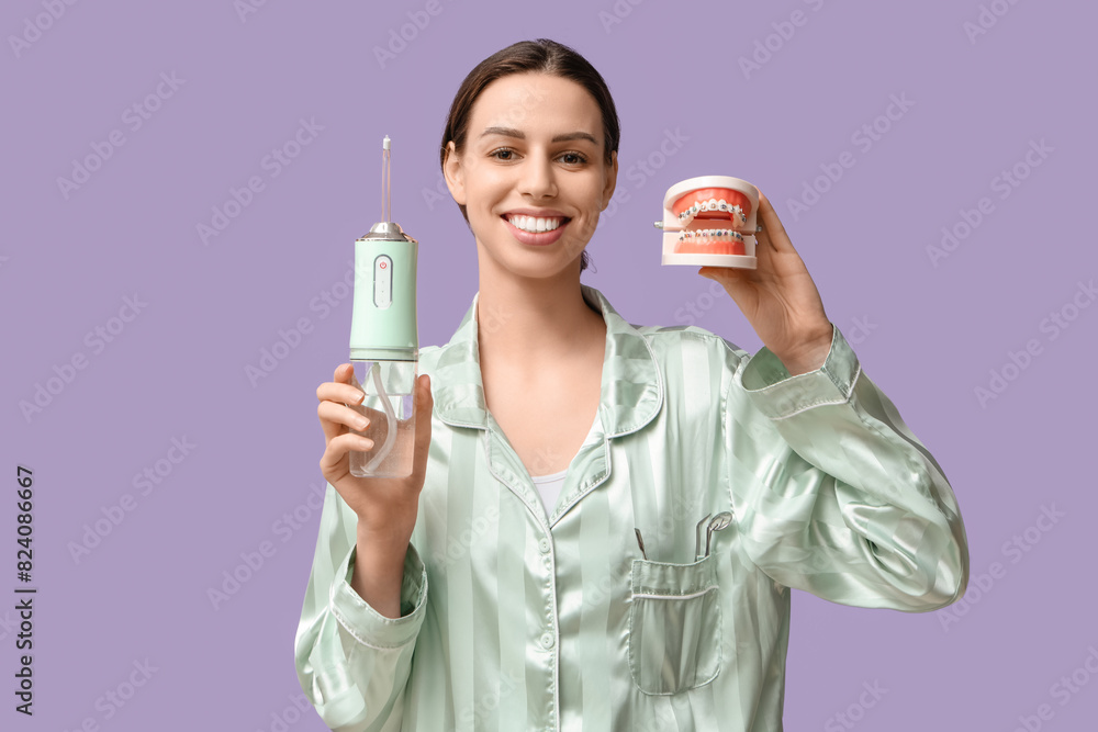 Beautiful young woman with oral irrigator and jaw model on lilac background Beautiful young woman with oral irrigator and jaw model on lilac background