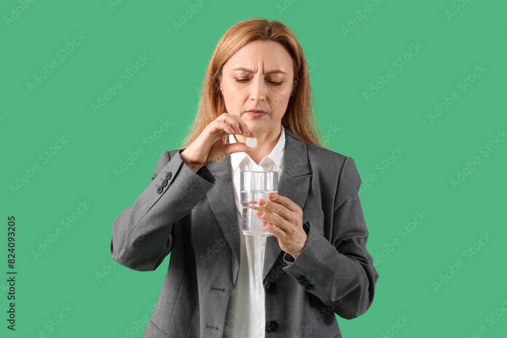 Adult woman suffering from headache with soluble tablet and glass of water on green background Adult woman suffering from headache with soluble tablet and glass of water on green background
