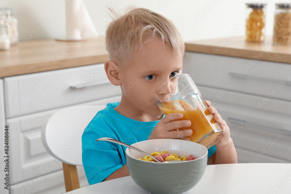 Happy little boy eating cornflakes with milk and drinking juice on breakfast at home Happy little boy eating cornflakes with milk and drinking juice on breakfast at home