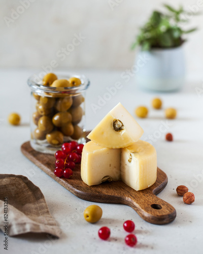 Caciotta cheese with olives on a wooden board, accompanied by red currants and a jar of olives