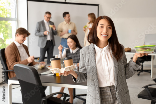 Young Asian businesswoman with coffee and sandwich during lunch in office