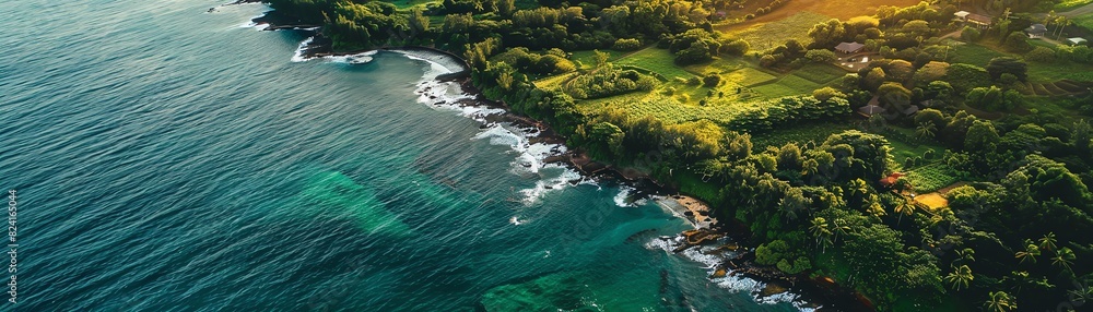 Aerial view of a picturesque coastline with lush greenery, clear waters, and waves crashing against the rocky shore at sunset.