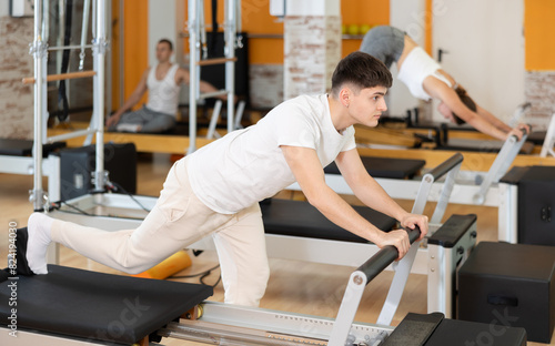 Man gym visitor performs reformer exercises aimed at stretching leg muscles and strengthening muscles of lower extremities. Pilates equipment in gym, classes for athletes and amateurs