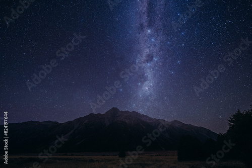 Starry Night Sky Above Mountain Range. The night sky is filled with countless stars shining above a majestic mountain range. The peaks of the mountains are silhouetted against the dark sky.