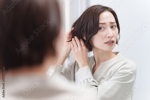 鏡を見て髪の毛を触るミドル女性（美容・ヘアセット・ヘアケア・髪の毛）