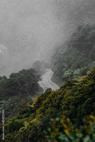 A foggy mountain landscape with a winding road cutting through the middle  disappearing into the mist. The road snakes its way up the mountain  disappearing around a bend in the distance.
