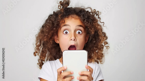 A young girl looks at her mobile phone with a surprised expression on her face