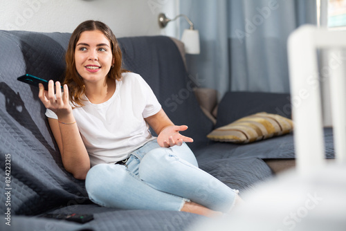 Young european woman, sitting on a sofa in an apartment, talking on a mobile phone with someone photo