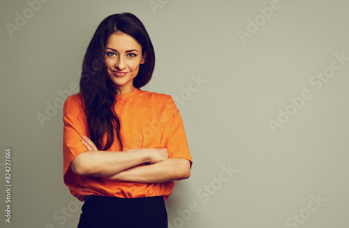 Beautiful young serious smiling business woman in bright casual orange t-shirt looking with folded arms on studio background on empty copy space. Closeup