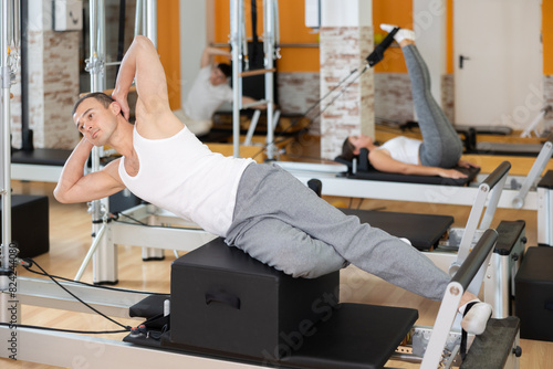 Man with help of informer is engaged in Pilates studio and performs exercises to strengthen muscles of press. Round-robin training for athletes during preparation for competitions photo