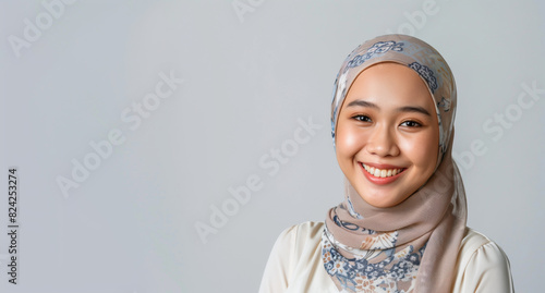A smiling young Malay woman in hijab with grey copy space