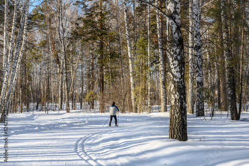 A ski run in a winter forest with snowdrifts and a skier under the bright sun