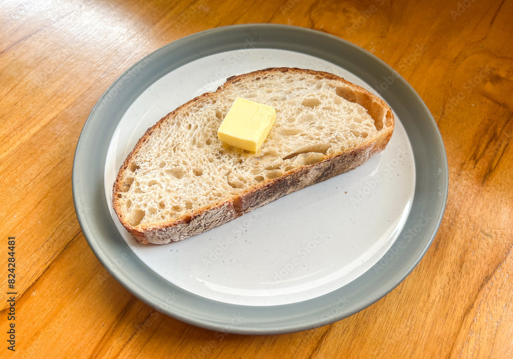 A piece of sliced sourdough bread on top with butter served on the plate.