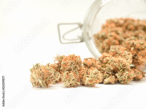 Dry cannabis buds outside of a jar on a white background.