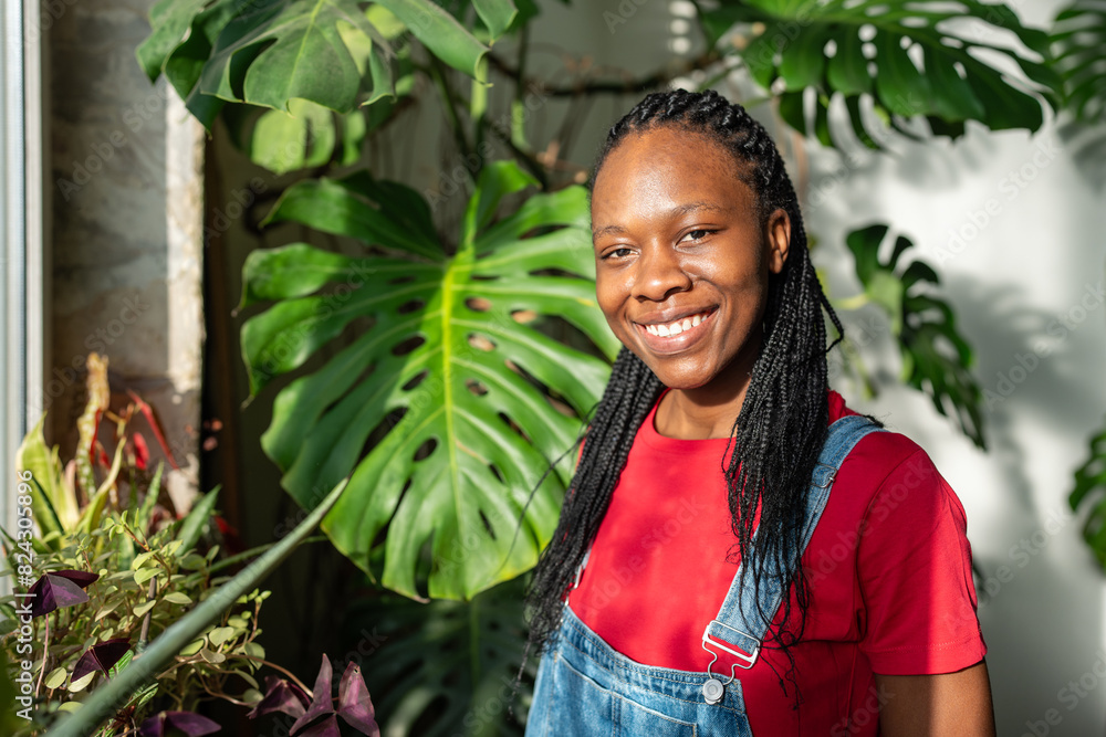 Satisfied happy african american girl gardener smiling looks to camera enjoy take care to indoor plants stands in greenhouse. Portrait pleased black young woman small business with houseplants owner. Satisfied happy african american girl gardener smiling looks to camera enjoy take care to indoor plants stands in greenhouse. Portrait pleased black young woman small business with houseplants owner.