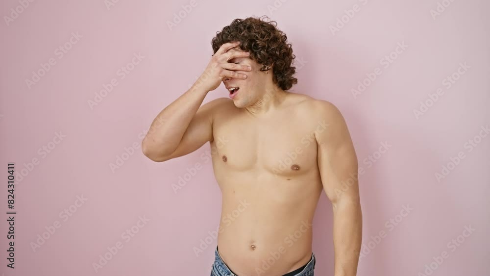 Shirtless young hispanic man, standing alone over pink background, shyly covers his face with a hand, peeking through fingers with a shocked expression and noticeable fear in his eyes. Shirtless young hispanic man, standing alone over pink background, shyly covers his face with a hand, peeking through fingers with a shocked expression and noticeable fear in his eyes.