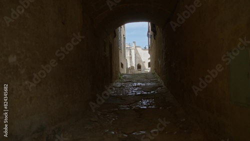 A narrow, cobblestone alleyway in matera, basilicata, italy, opens up to bright daylight revealing ancient stone buildings characteristic of historic european architecture. photo