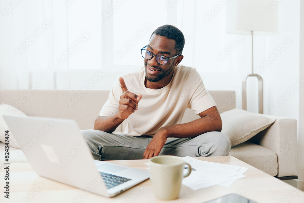Smiling African American Freelancer Working on Laptop on Sofa in Modern Home The young black guy is typing on his computer, enjoying his work in the cozy living room With a relaxed and cheerful Smiling African American Freelancer Working on Laptop on Sofa in Modern Home The young black guy is typing on his computer, enjoying his work in the cozy living room With a relaxed and cheerful