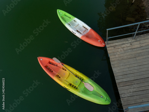 Colorful rainbow-striped kayak resting on the calm water. Secured to a wooden dock made of weathered planks of a lake