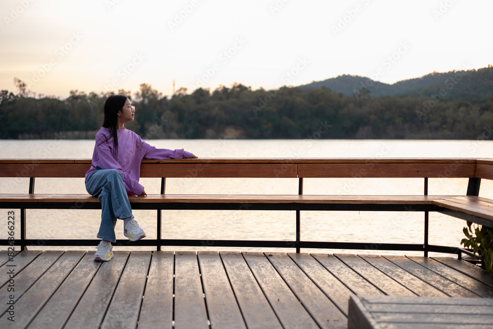 Asian girl sitting and enjoying the morning scenery by the lake with mountains