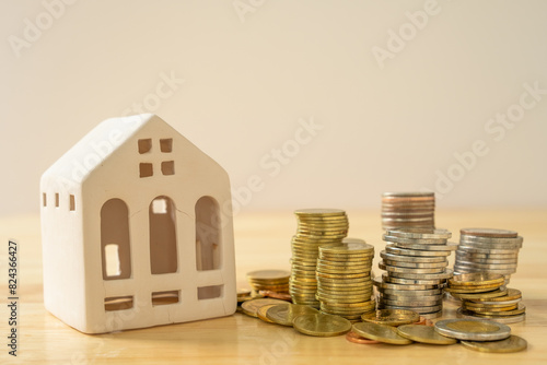 A house model and coins are placed on a wooden table with copy space. Concepts of finance, banking, loans and buying-selling or mortgaging real estate.