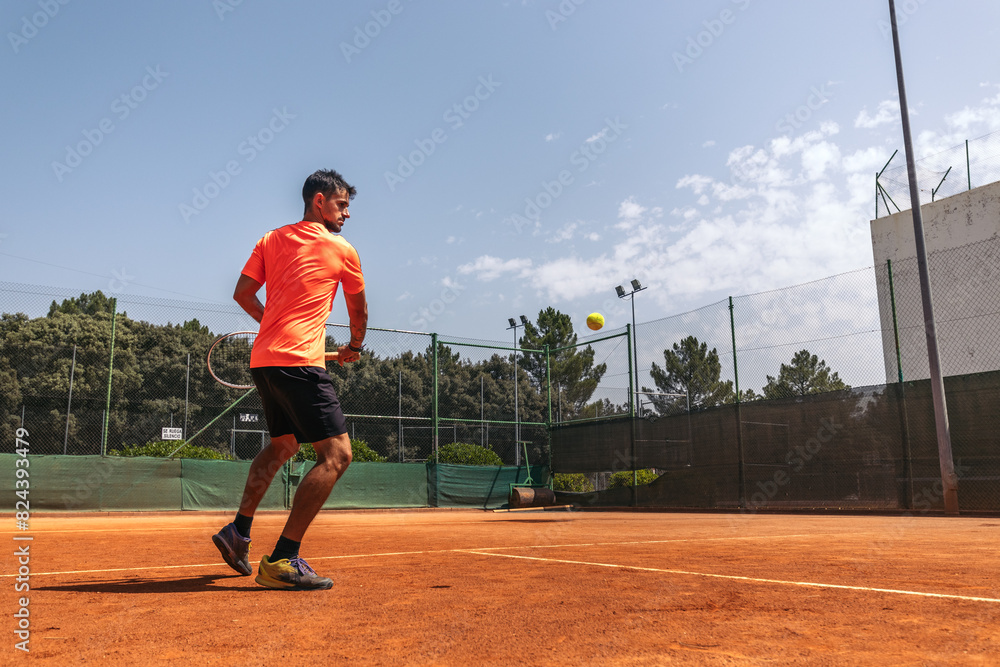 Obraz premium Man in sportswear playing tennis on a dirt tennis court