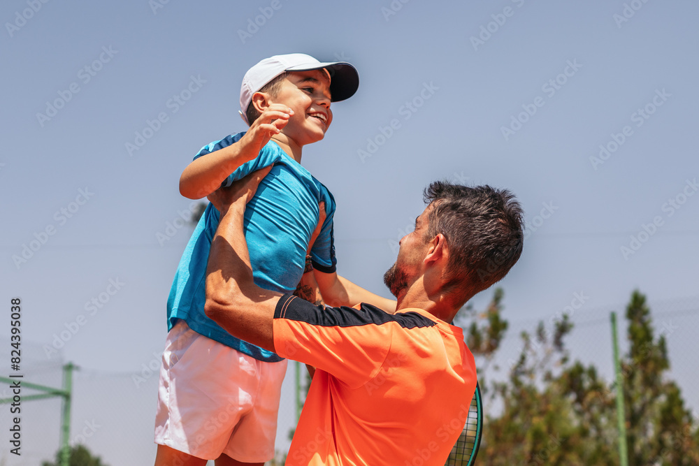 Naklejka premium Father and son playing tennis together on a dirt court