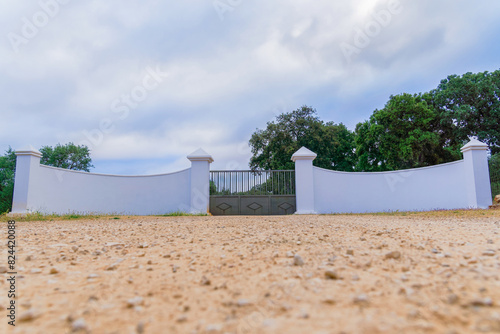 entrance to an agricultural and livestock farm with white walls and a metal gate with a cloudy sky in the background.