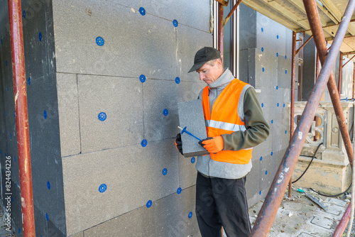 Installation of thermal insulation on the external walls of a house. Thermal coat to improve the energy efficiency of the house. Worker holding a panel of polystyrene thermal cladding 