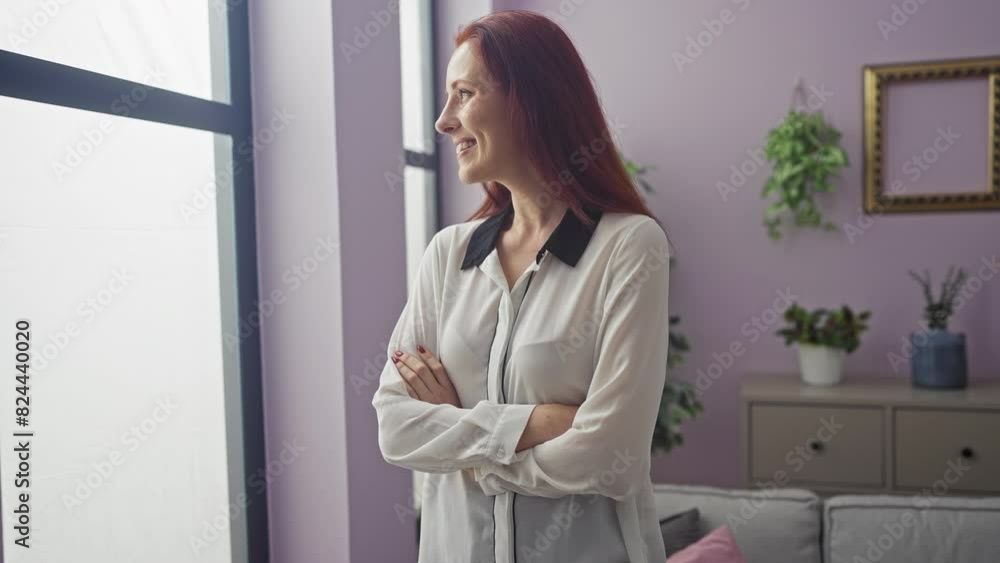 Redhead woman with arms crossed standing smiling in a cozy, modern living room. Redhead woman with arms crossed standing smiling in a cozy, modern living room.