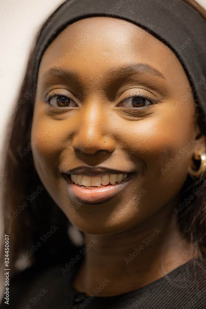 This image features a close-up portrait of a smiling Black woman wearing a black headband. Her dark, expressive eyes and radiant smile are the focal points of the image, highlighting her natural This image features a close-up portrait of a smiling Black woman wearing a black headband. Her dark, expressive eyes and radiant smile are the focal points of the image, highlighting her natural