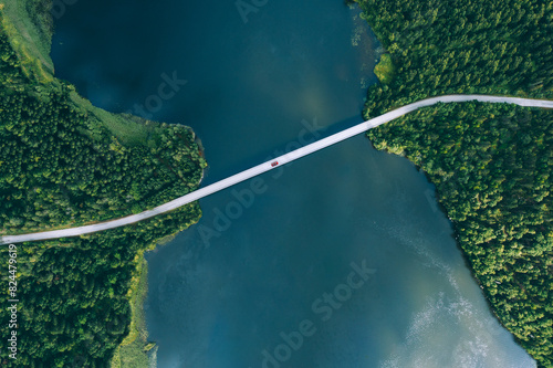 Aerial view of bridge road with red car over blue water lake or sea with island  and green woods in Finland.