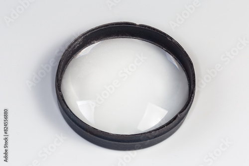 Old simple plano-convex metal frame lens on gray background