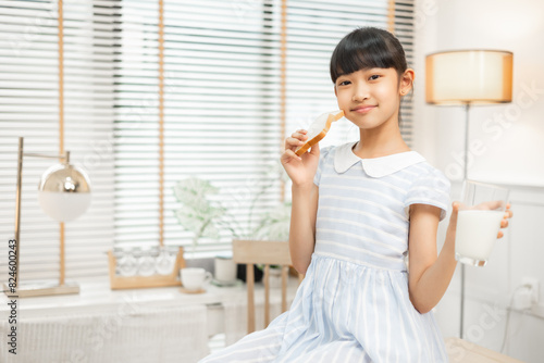 Daughter enjoying breakfast with milk in a warm, inviting kitchen.Asian family breakfast scene, parents and daughter eating and drinking milk at home.