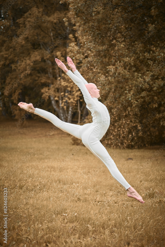 Full length portrait of young hairless girl ballerina with alopecia in tight white suit jumps on fall lawn in park, symbolizing overcoming challenges and gracefully acceptance individuality