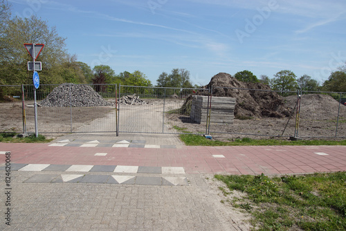 Building site, which is being prepared for construction behind a fence with piles of earth, tiles, stones, tree stumps. In the Dutch village of Bergen. Spring, May, Netherlands photo