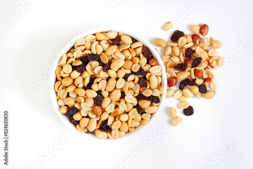 Peanut and raisin mix in round white bowl, isolated on white with loose bits around the bowl, with copy space