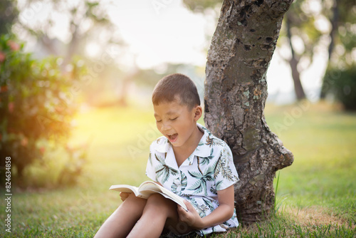 Little boy reading a book under big tree