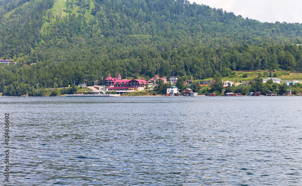 View from the water of the wooded shore of Baikal Lake and the village of Listvyanka in the distance. Summer trips on the lake by boat and outdoor recreation View from the water of the wooded shore of Baikal Lake and the village of Listvyanka in the distance. Summer trips on the lake by boat and outdoor recreation