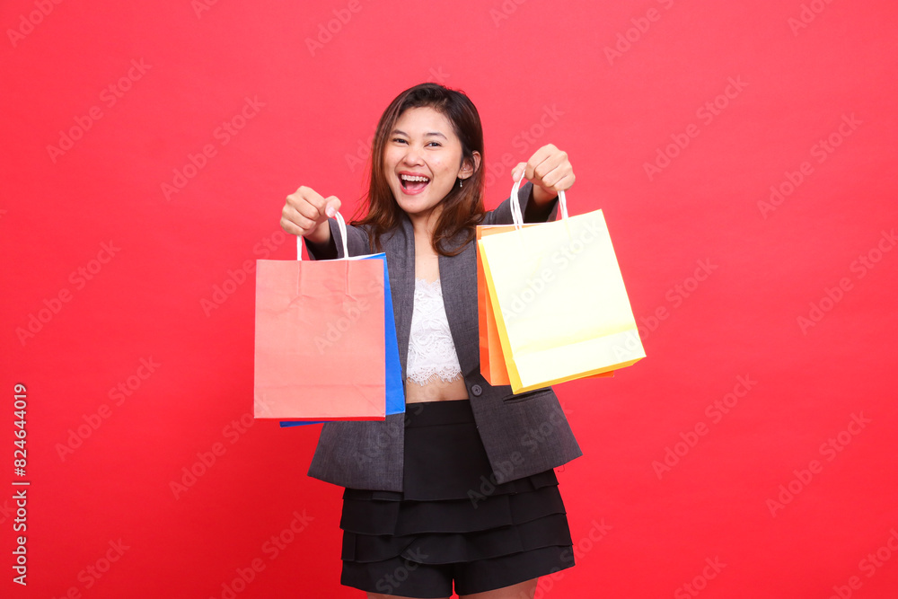 Portrait of a cheerful, happy Asian office woman with both hands raising a shopping paper bag in front of her wearing a formal jacket on a red background. for transaction, lifestyle and business Portrait of a cheerful, happy Asian office woman with both hands raising a shopping paper bag in front of her wearing a formal jacket on a red background. for transaction, lifestyle and business