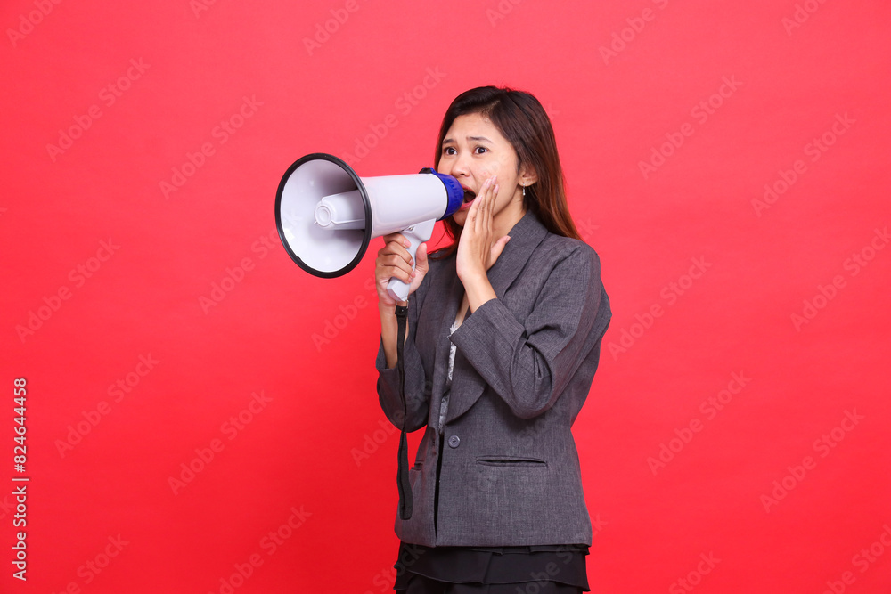 indonesia office girl expression tilted top right shouting angrily using a megaphone hand focusing candid voice wearing gray jacket and skirt on red background. for broadcast, business and advertising indonesia office girl expression tilted top right shouting angrily using a megaphone hand focusing candid voice wearing gray jacket and skirt on red background. for broadcast, business and advertising