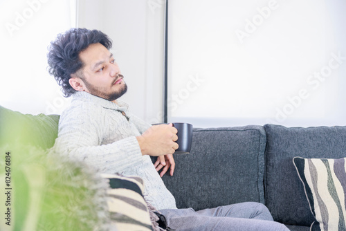 ソファーに座り、暖かい飲み物を飲む男性 photo