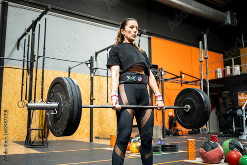 A middle-aged woman is weightlifting inside a large gym.The 50-year-old woman deadlifts to work her back and quads.Concept of senior women doing sports.