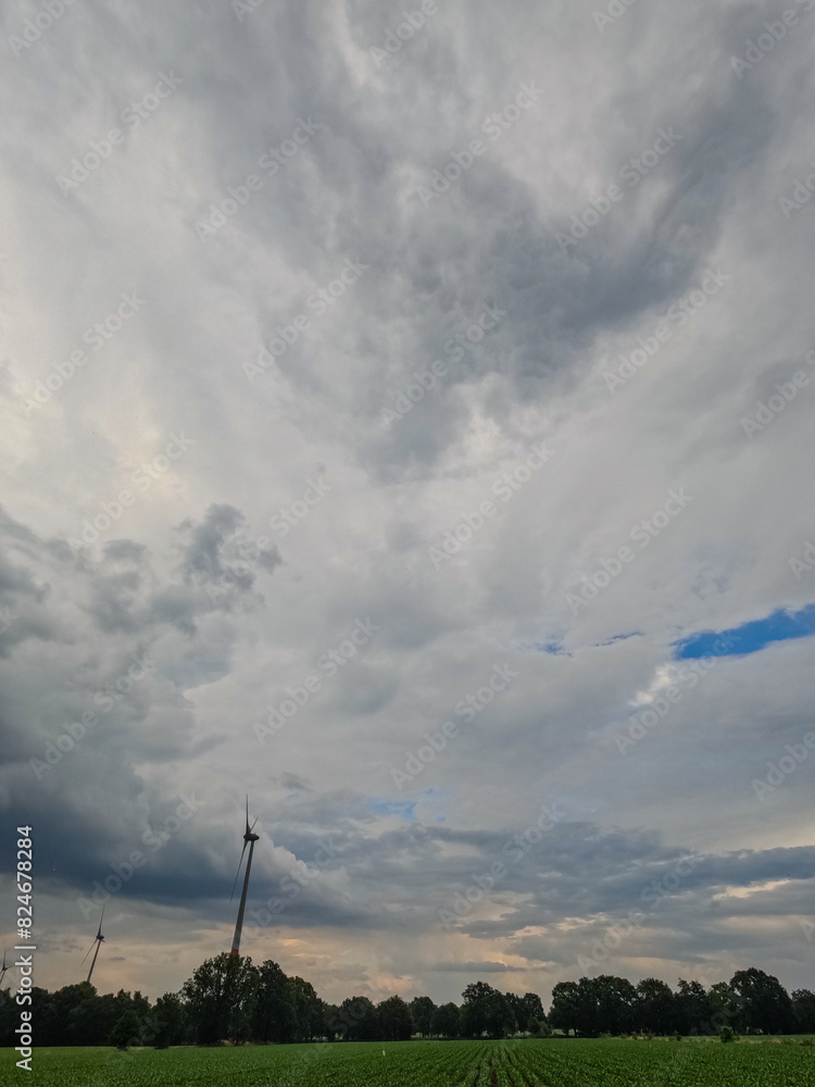 A cloudy sky with wind turbines overlooks a green field, harnessing renewable energy in a stunning natural setting A cloudy sky with wind turbines overlooks a green field, harnessing renewable energy in a stunning natural setting