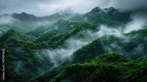 Lush forested mountain range shrouded in mist, with waterfalls cascading among the greenery on a cloudy day.