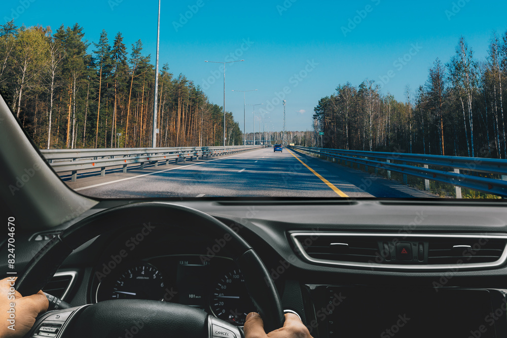 Hands of car driver on steering wheel. Man driving car on asphalt highway road in summer Finland.